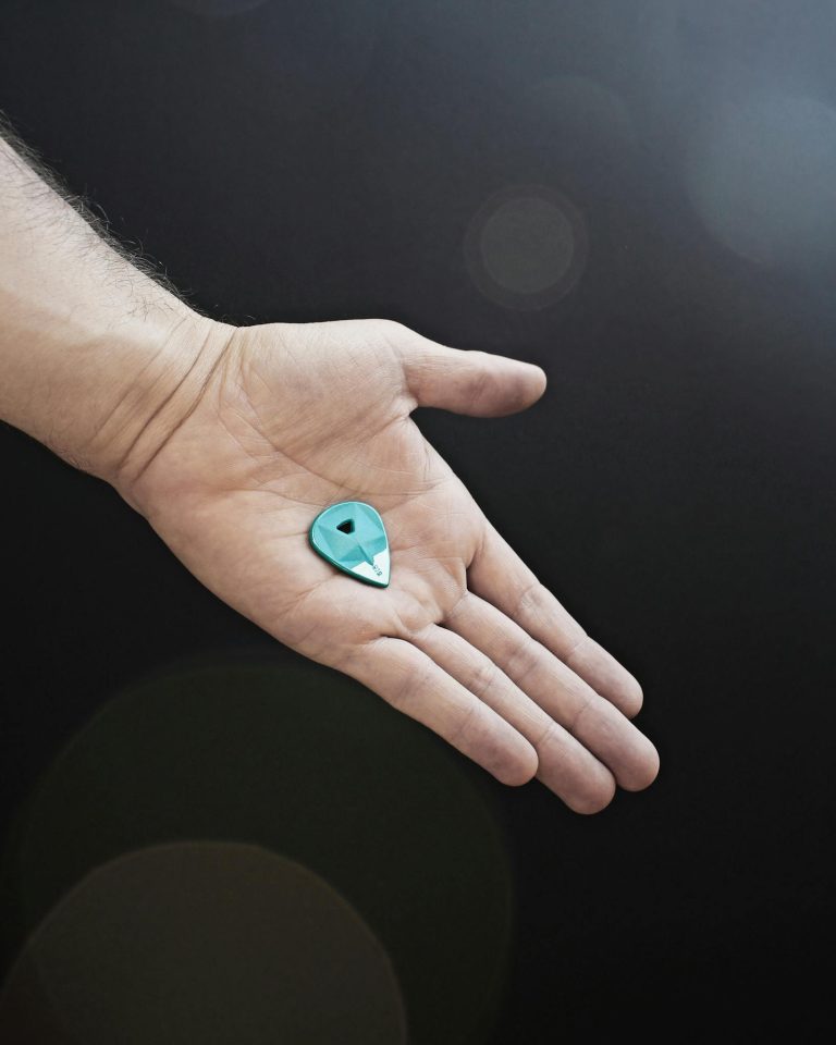 A close-up shot of a person's hand holding a blue guitar pick against a dark background.